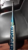 Full view of the Louisville Slugger bat showing the barrel and handle wrapped in black grip tape on a gray chair.