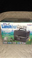 Top and front side of the Lunchbox Stove box showing 12V Lunchbox Stove branding and image of the product with its lid closed, handle visible.