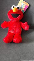 Full view of the Mini Tickle Me Elmo plush toy, red with orange nose and large eyes, showing good condition and tag attached.