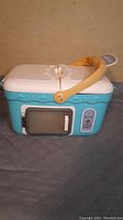 Toy kitchen microwave oven, light blue with white top and brown handle, showing the front with door and buttons
