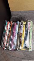 Photo showing 11 unopened DVDs stacked in a box, titles including horror, comedy, and fantasy movies.