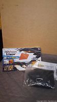Photo of the HDVision Visor box along with a black pouch and metal clip in plastic bag laid out on surface, packaging shows wear.