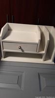Closed view of white wooden desk organizer showing the drawer front and compartments