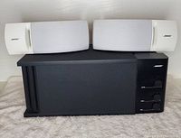 Front view of the Bose Acoustimass 3 subwoofer with the two Bose 161 bookshelf speakers placed on top showing their white grills and Bose logo.