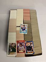 Box filled with large stacks of baseball cards, showing a few cards with player images on the top including one of a batter in swing pose and another of a pitcher.