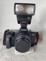 Front view of Canon EOS 650 camera with Speedlite flash attached and 50mm lens with lens cap on.