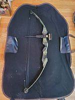 Top view of the olive green Pro Line compound hunting bow laid on a black fabric inside the camouflage carrying case.