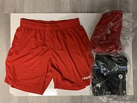 Three pairs of women's soccer shorts: one red pair out of package, one red and one black pair inside plastic packaging placed on a white surface.