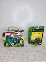 Mini tin lunchbox and sealed die cast John Deere tractor on neutral background.