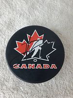 Top view of black hockey puck with red and white maple leaf and hockey player silhouette logo and John Tavares autograph on top.