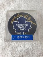 Top side of puck showing Toronto Maple Leafs logo and Johnny Bower autograph in gold ink.