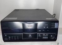 Front view of the Kenwood DVD/CD changer showing the disc tray, control buttons, progressive scan label, and partial label on the display.