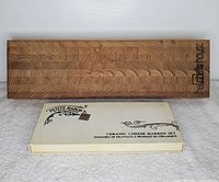 Long rectangular wooden cheese board with intricate end grain wood pattern and brand engraving.