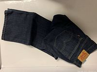 Folded view of dark blue Levi's jeans showing rear pocket with leather patch label and red tab.
