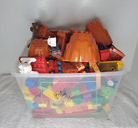 Transparent storage bin filled with assorted large plastic building blocks with a focus on large brown pieces at the top resembling mountain blocks.
