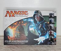 Front of the Magic The Gathering: Arena of the Planeswalkers board game box, showcasing artwork of a blue-robed Planeswalker casting a spell, logo, and game details.