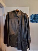 Front view of the black men's leather jacket hanging on a hanger, showing full length, collar, and pockets.