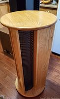 Photo showing entire wooden rotating CD storage tower with a natural oak finish, vertical black CD racks, circular top and base on a wooden floor.