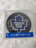 Top view of the hockey puck with the Toronto Maple Leafs logo and Tomas Kaberle's autograph in gold ink inside a clear display case with label