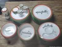 Full set of vintage Baldelli ceramic dishes including spaghetti plates, pasta bowls, artichoke plates, espresso mugs, and mini saucers arranged on a wooden table showing their handwritten style text and colorful rims