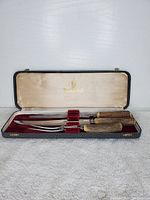 Full view of the carving set inside the open case, showing the knife, fork, and sharpening steel with wooden handles and the maroon and cream satin lined case.