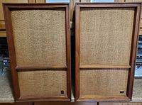 Front view of the pair of vintage Wharfedale speakers showing the woven fabric grills and solid wood frames with wear and aging visible.