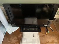 Front view of the 22 inch Sony LCD TV area showing the screen, remote control, and user manual on a wooden desk.