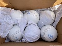 Photo showing six white leather Top-Flite branded softballs in tissue paper inside the box.