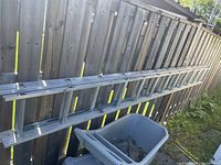 Photo of a 26-foot aluminum extension ladder leaning against a wooden fence outdoors, showing the full length and condition of the ladder.