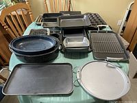 Top view showing assortment of baking and roasting pans, muffin trays, pizza pan, and grill pan arranged on a table.