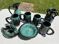 Photo showing four Blue Mountain Pottery mugs with star pattern, decorative bowl, swan-shaped piece, and double-handled vase on white table outdoors.