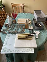 Overview of entire kitchen utensil lot on table including cutting boards, knives, spatulas, and utensil holder.