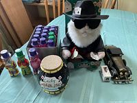 Overview photo showing lot contents including 17 colorful bingo markers, black gamblers jar, Kenny Rogers singing doll dressed as gambler, and two toy cars (one large battery operated and one mini car boxed)