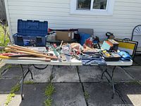 Wide view of all tools spread out on a table including toolbox, axes, saws, drills and other tools