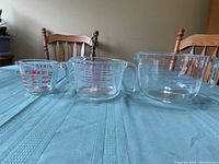 Three Pyrex glass measuring cups of small, medium, and large size displayed on a table.