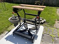 Front and side view of the Black & Decker Workmate 200 workbench showing wooden top clamping surfaces and folding steel frame on a sunny outdoor background.