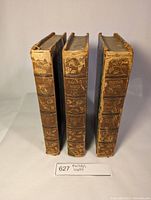 Three leather-bound volumes of Macaulay's Works from 1866 with gold embossed floral designs on spine and volume titles and numbers.