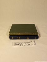 Two hardcover books stacked; the top one is green with gold embossing spine, bottom one dark blue with gold lettering spine.