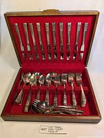 Closed view of entire flatware set inside a wooden case lined with red velvet, showing knives vertically and other utensils in lower slot.