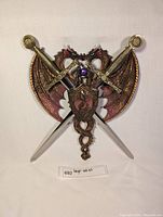 Twin dragon wall art featuring two dragons with spread wings, crossed swords with gold-colored handles, a purple orb, and a detailed shield centerpiece with dragon motif.