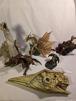 Collection of dragon figurines and large gargoyle shown on a white backdrop, some damaged or incomplete