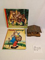 Two German children's books lying side by side and a Bavarian style house music box made of wood.