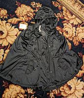 Full view of black Lululemon poncho jacket with hood spread on patterned carpet, showing drawstring at waist and snap buttons.