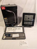 Photo of Globe LED desk lamp box, Accurite weather station, and Mastercraft digital calipers case open with calipers inside