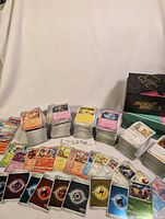 Multiple stacks of Japanese Pokémon cards with visible character and energy cards in front of two Pokémon trading card game boxes.