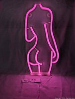 Pink LED neon sign lit against dark background showing full side profile of a woman's body silhouette.