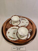 Two fine bone china teacup sets displayed on a round copper tray, showing full arrangement and detail of patterns.