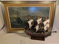 Front view of framed ship picture with decorative sail ship in front, showing details and scale of both items.