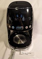 Front view of black SMEG drip coffee machine showing brand name and control buttons.