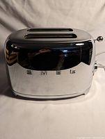 Front view of SMEG stainless steel toaster with visible SMEG branding and reflective surface.